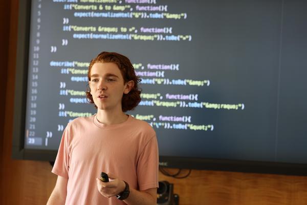 Student presenting in front of a screen of code