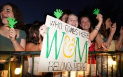 Students cheering at night holding hand clappers and a sign that reads "Who Comes Here Belongs Here"