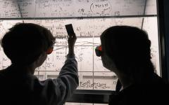 Silhouette of two students looking at white board with equations written on it