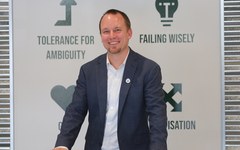 Graham Henshaw smiles in front of an Entrepreneurship Hub wall listing skills like “failing wisely.”