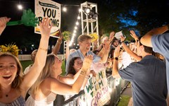 Cheering students high-five each other under string lights at Convocation