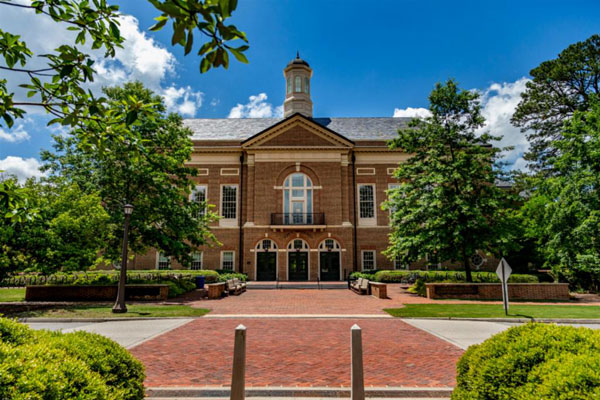 Miller Hall, a grand three-story brick building with cupola, framed by green trees, a wide brick walkway and a blue sky
