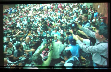 Slide 22: A large group of people, mostly journalists with cameras and microphones surrounded and centered on one person