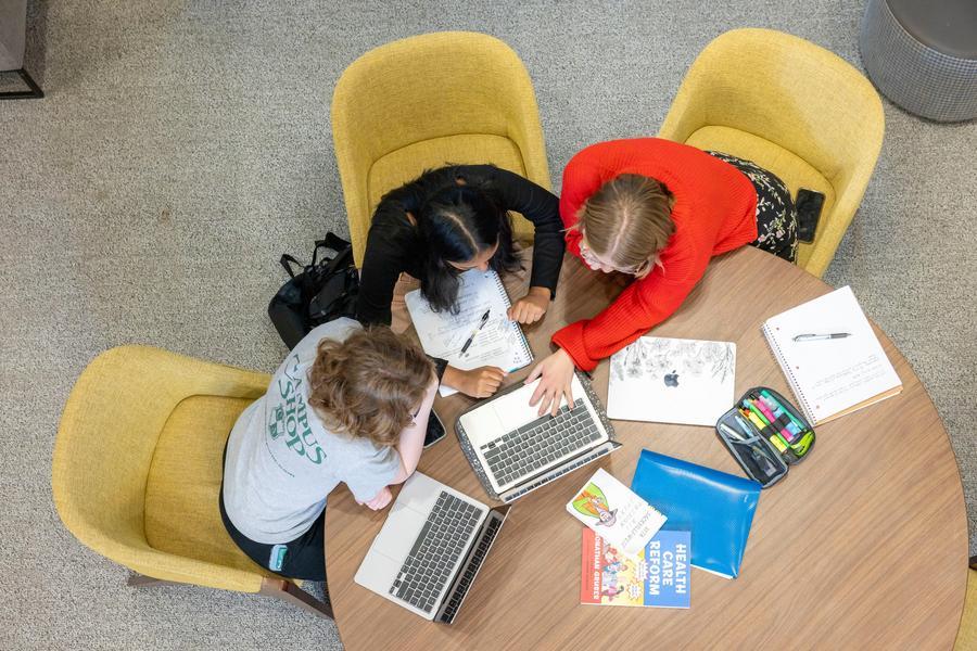 Image from above showing three students working together at a table with a laptop and notebooks