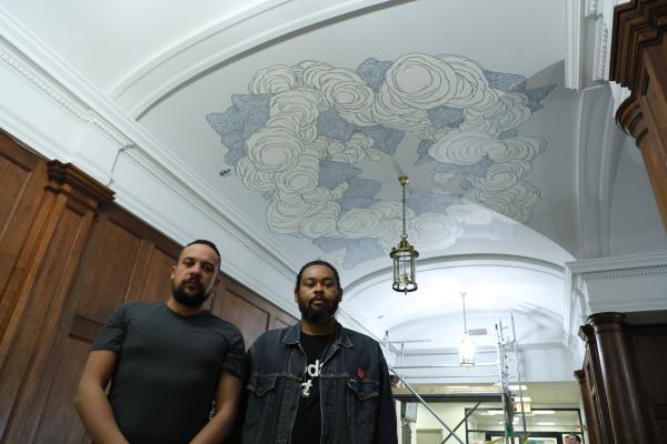 Reunion Island artists Kid Kreol and Boogie pose underneath their mural on the Washington Hall lobby ceiling