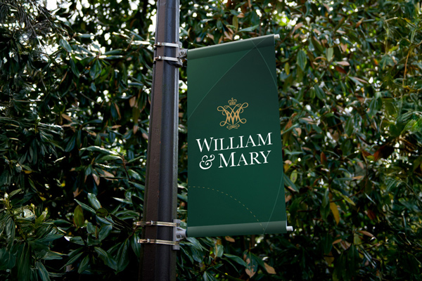 A lightpost banner with the W&M secondary logo with cypher on a green background with curved lines
