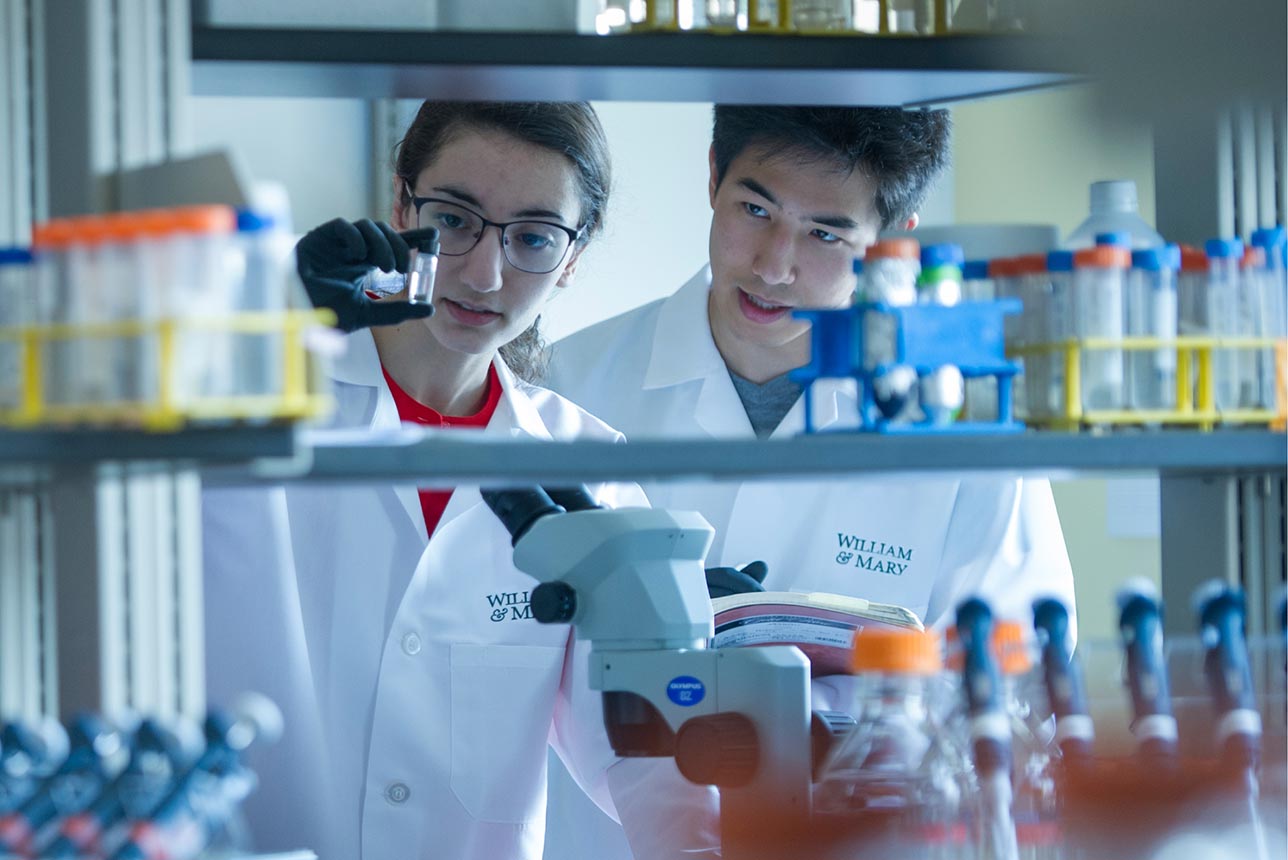 Two students in a science lab framed by a shelf of lab equipment