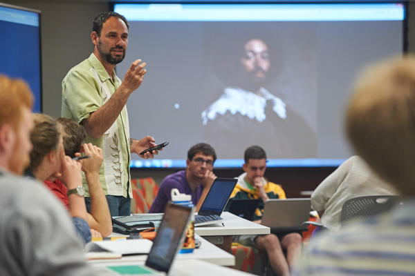 A professor stands in front of a full classroom of students