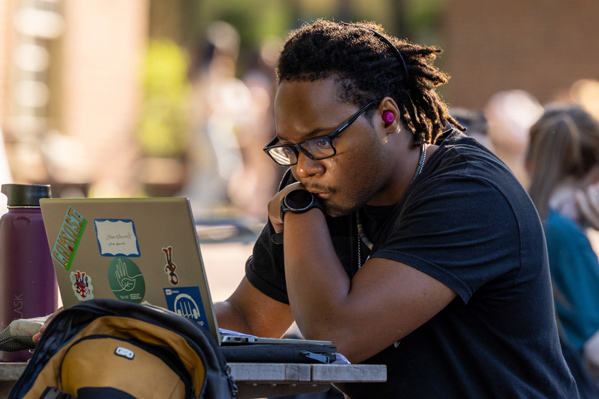Male student looking at laptop outside