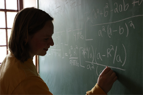 Student writing math equation on green chalkboard