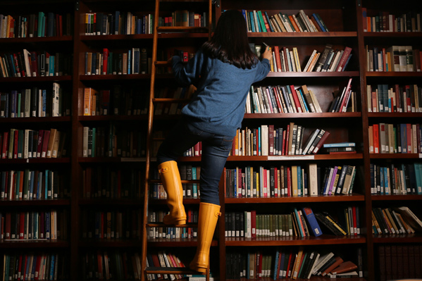 Student climbing a ladder in front of colorful bookshelves