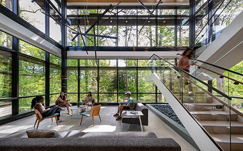 Several students sitting in the two story glass atrium of the Wellness Center, overlooking the woods behind the building.