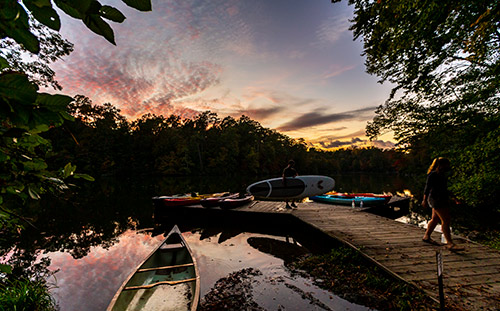 Students, kayaks and canoes on the dock at Lake Matoaka at sunset