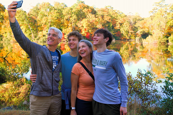A smiling family taking a selfie by Lake Matoaka with vivid fall foliage