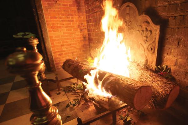 Yule logs burning in a large brick fireplace with sprigs of holly tossed around the logs