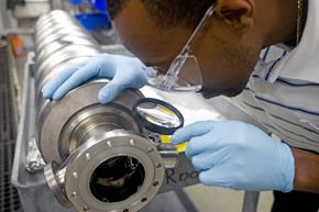 A Jefferson Lab technician examines an RF cavity. The particle accelerator at JLab contains more than 300 of these superconducting components. Jefferson Lab photo