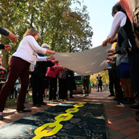 Attendees hold paper aloft in preparation for pressing it down onto the woodcut block. (Photo by Stephen Salpukas)