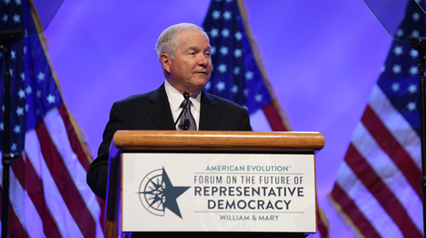 Robert Gates stands behind a podium with flags behind them