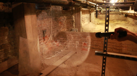 A hand shines a flashlight at a brick wall in the basement of the Wren Building where a vaulted drain leads outside