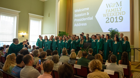 The W&M Choir wearing green robes performs in front of a crowd