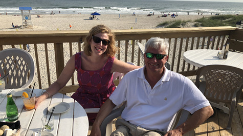 Ali Gaidies Joy and Austin Joy sit on a deck in front of a beach