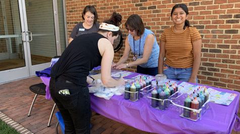 Four people work around a table with paint bottles and other crafting supplies