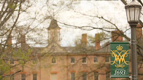 A banner with the William & Mary cypher and 1693 on it hangs on a lightpole in front of the Wren Building