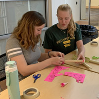 Two students work on a crafting project together while sitting at a table