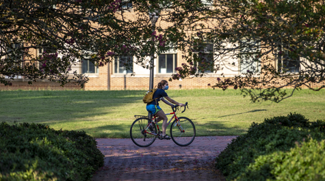 A student rides a bicycle through campus