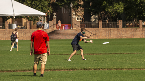 Students wearing masks play Frisbee