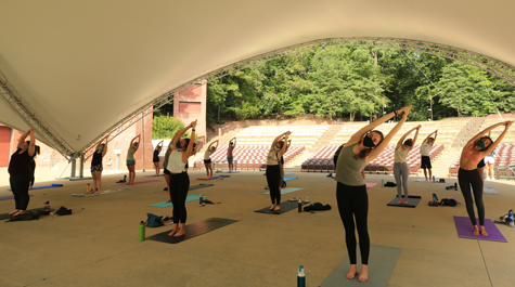 Students wearing masks stretch with their arms extended upward while doing yoga
