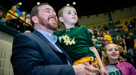 A person watching a basketball game laughs while holding a small child