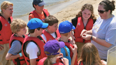 Children wearing life jackets surround an adult on a beach