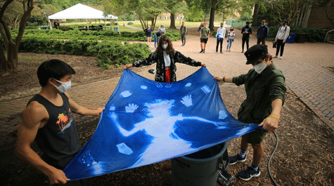 Three students hold different edges of a cloth dyed blue with white images on it