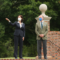 Two people wearing masks and suits stand at the top of steps outside