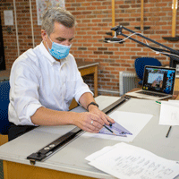 Matthew Allar draws at a drafting table with camera overhead