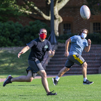 People wearing masks run on a grassy field in pursuit of a rugby ball