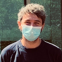 Researcher stands outside his lab's building with mask on