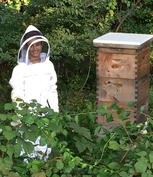 A person in a bee keeper suit stands near a hive