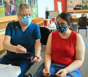 W&M alumna Diane Seager (left), who is volunteering at the Greater Williamsburg clinic, shows a vaccination card to Christina Marlow, a graduate student in psychology. (Photo by Stephen Salpukas)