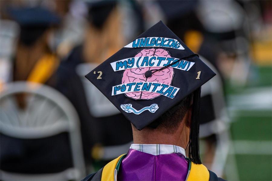 A graduating student wears a cap with a depiction of a brain that reads: unlocking my action potential.