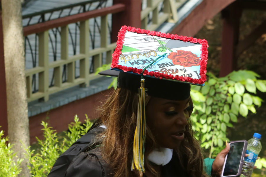 A graduating student wears a cap that reads: I am the rose that grew from concrete.