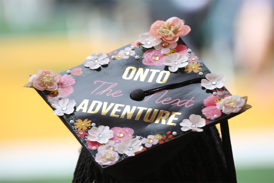 A mortarboard decorated with flowers and words saying, On to the next adventure.