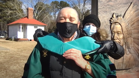 A person places an academic hood on Warren Cook, who wears academic regalia