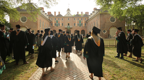People in caps and gowns walk toward a large brick building