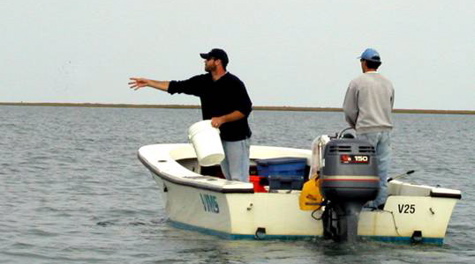 A person in a small boat throws something into the water from a bucket
