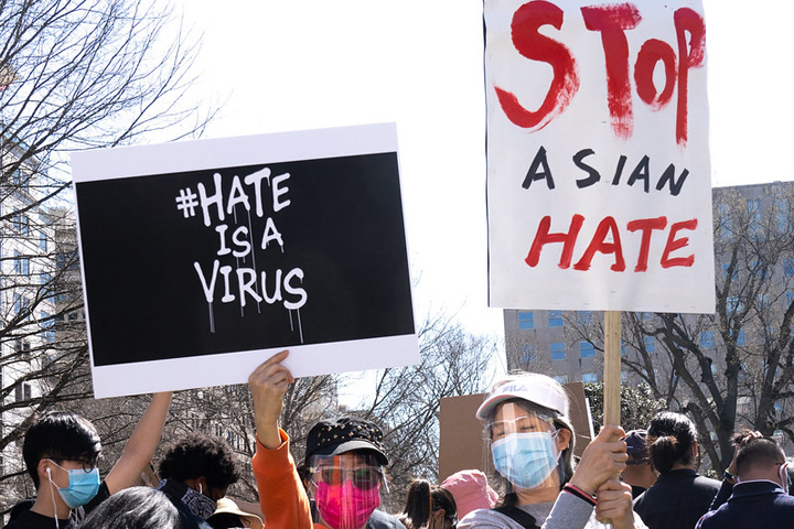 Two people hold up signs that say Hate is a Virus and Stop Asian Hate