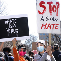 Two people hold up signs that say Hate is a Virus and Stop Asian Hate