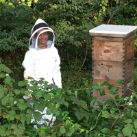 A person in a bee keeper's suit stands near a hive