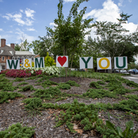 Signs in a flower bed spell out Welcome, W&M Loves You
